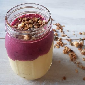 Nicecream met mango en kersen in een grote glazen Mason Jar. De Nicecream is gegarneerd met granola.