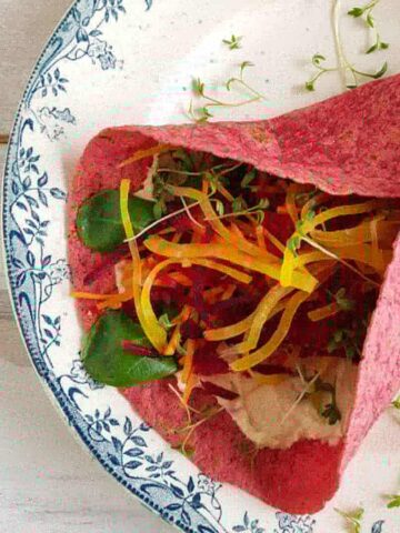 Bietenwrap: een kleurrijke rode wrap met hummus en groenten, op een bordje.