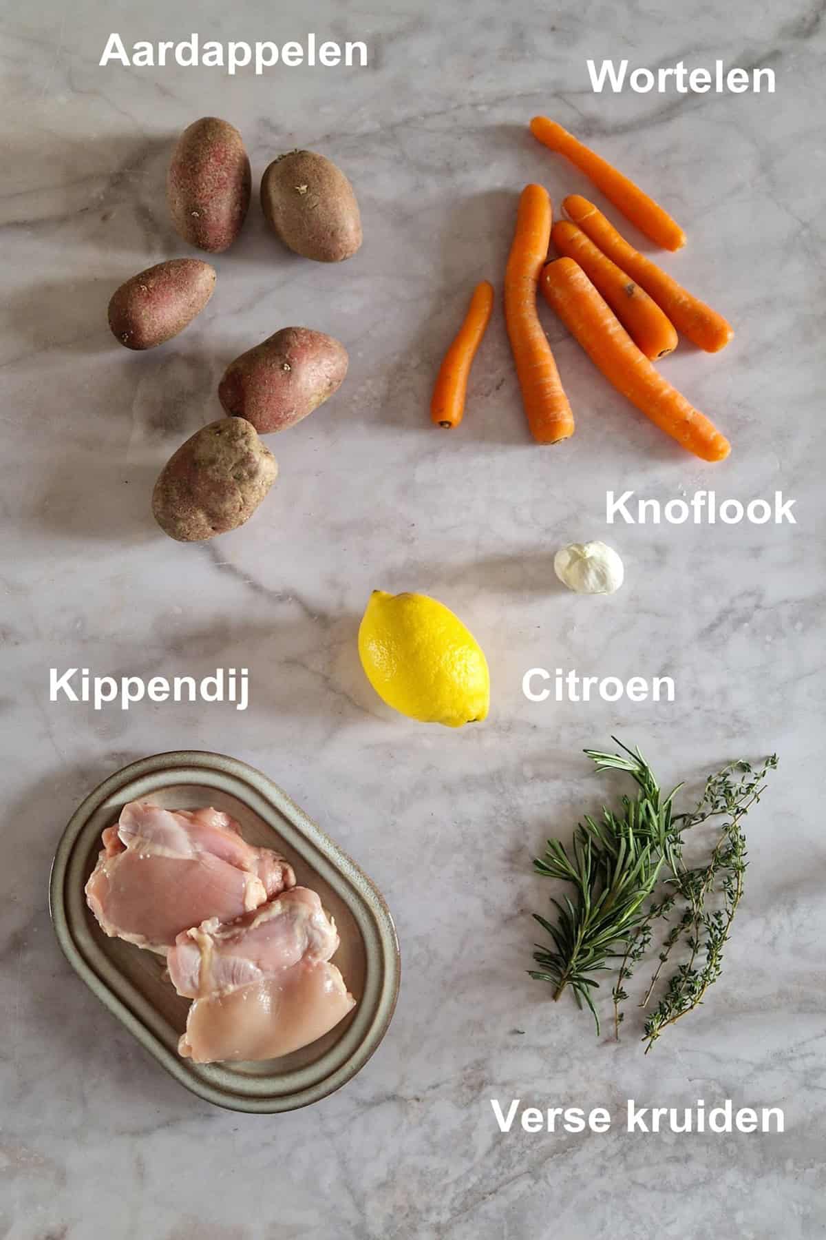 De ingrediënten voor een kip traybake, uitgestald op een lichte, marmeren ondergrond.