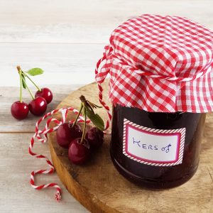 Zelf jam maken: een potje zelfgemaakte kersenjam. Er zit een handgemaakt label op de pot en er liggen verse kersen omheen.