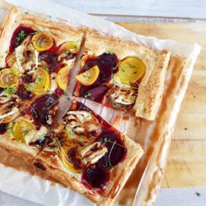 Plaattaart met bietjes en brie, op een grote houten serveerplank met bakpapier eronder.