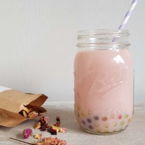 Rozen bubble tea in een grote Mason Jar. Er liggen gedroogde roosjes naast om de smaak van de bubbletea aan te geven.