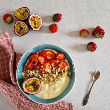 Een mango smoothiebowl met aardbeien, granola en een halve passievrucht als garnering.