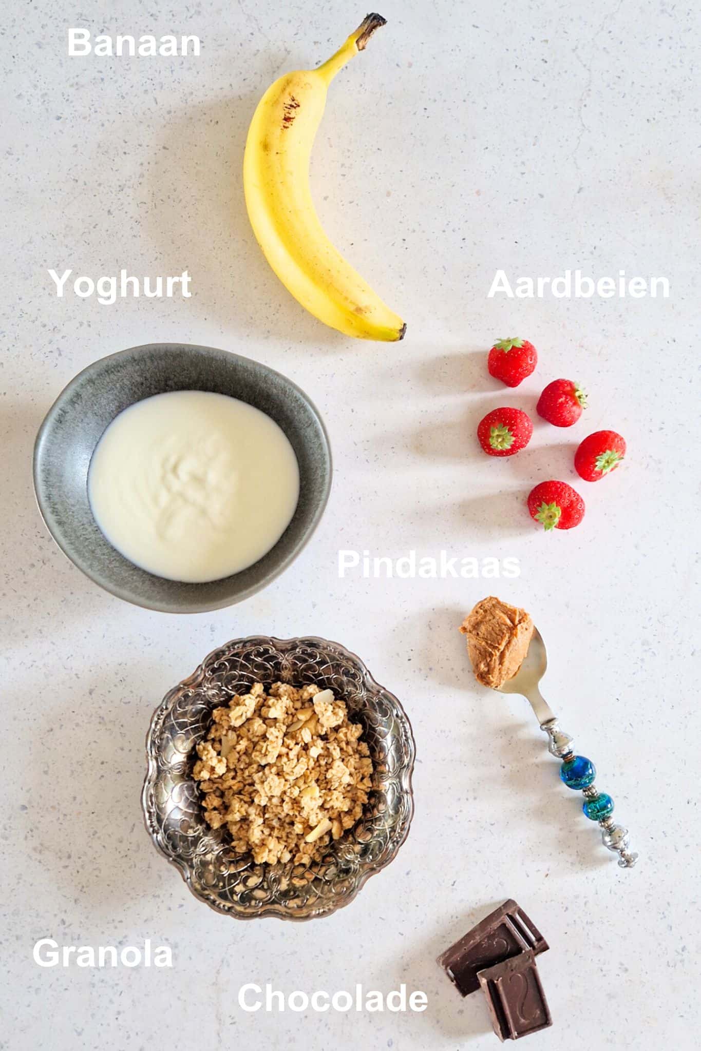 De ingrediënten voor een smoothiebowl banaan: een banaan, yoghurt of kwark, aardbeien, pindakaas, granola en chocolade.