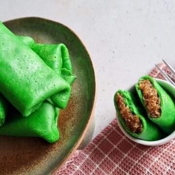 Pandan pannenkoeken op een bordje, met ernaast een opengesneden exemplaar zodat je de kokosvulling goed kunt zien.