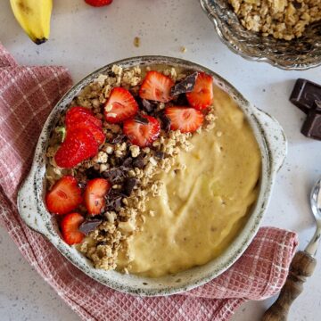 Een smoothiebowl met banaan en pindakaas. De smoothiebowl is afgetopt met granola, aardbeien en stukjes grof gehakte chocolade.
