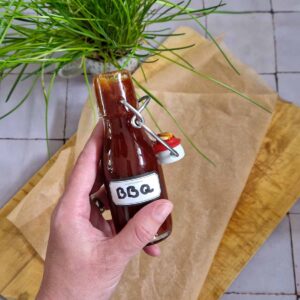 BBQ saus zelf maken: een hand houdt een flesje zelfgemaakte barbecuesaus omhoog.