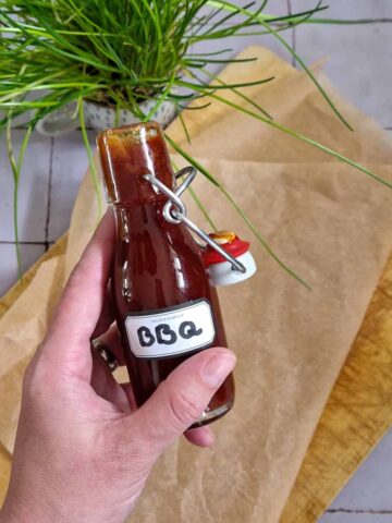 BBQ saus zelf maken: een hand houdt een flesje zelfgemaakte barbecuesaus omhoog.