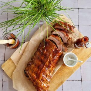 Spareribs uit de oven met een kleverige glazuurlaag, op een vel bakpapier. Ernaast staan verschillende sausjes.