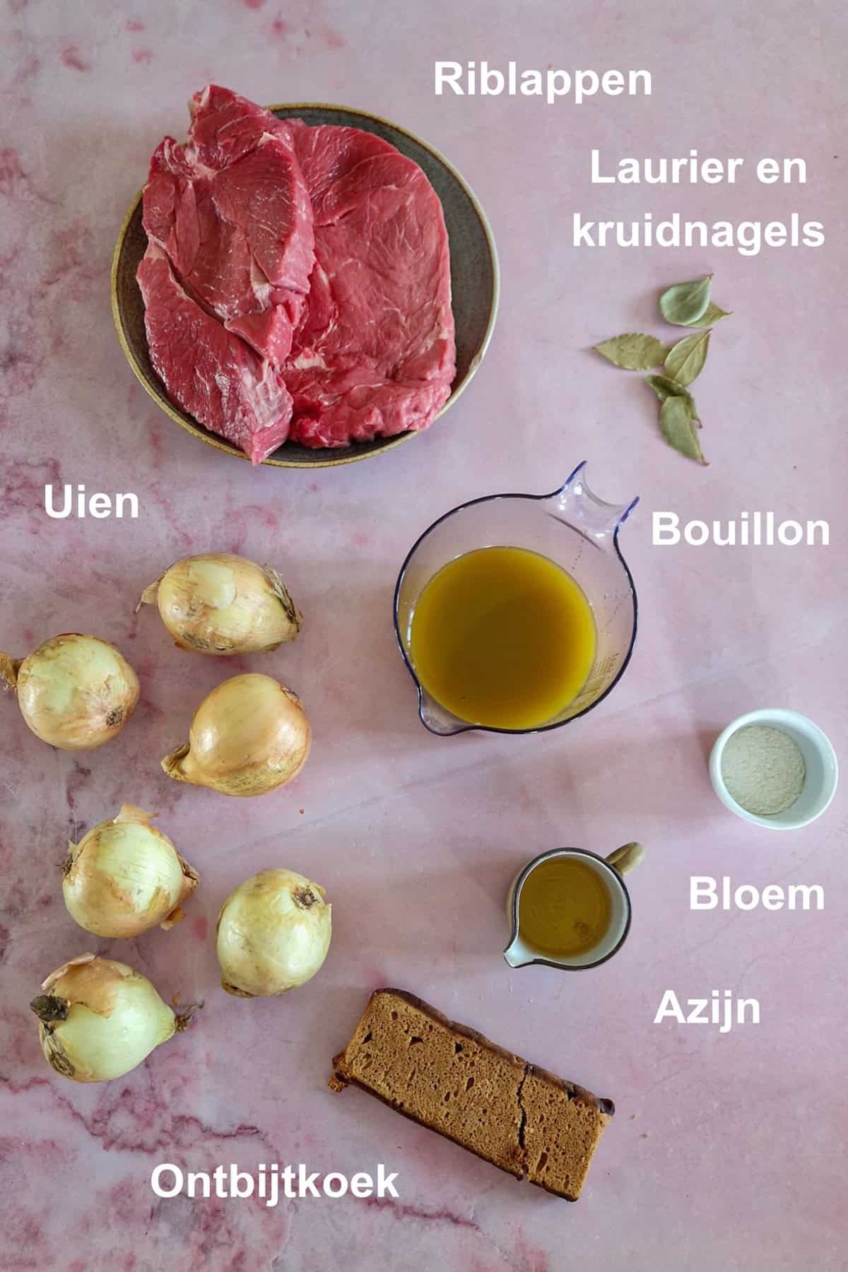 De ingrediënten om ouderwetse hachee te maken, uitgestald op een lichtroze marmeren ondergrond. Bij elk ingrediënt staat met tekst vermeld wat het is.