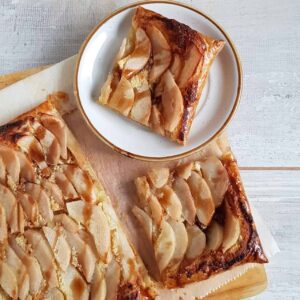 Peren - frangipanetaart op een grote houten plank met bakpapier. Uit de taart zijn twee punten gesneden.