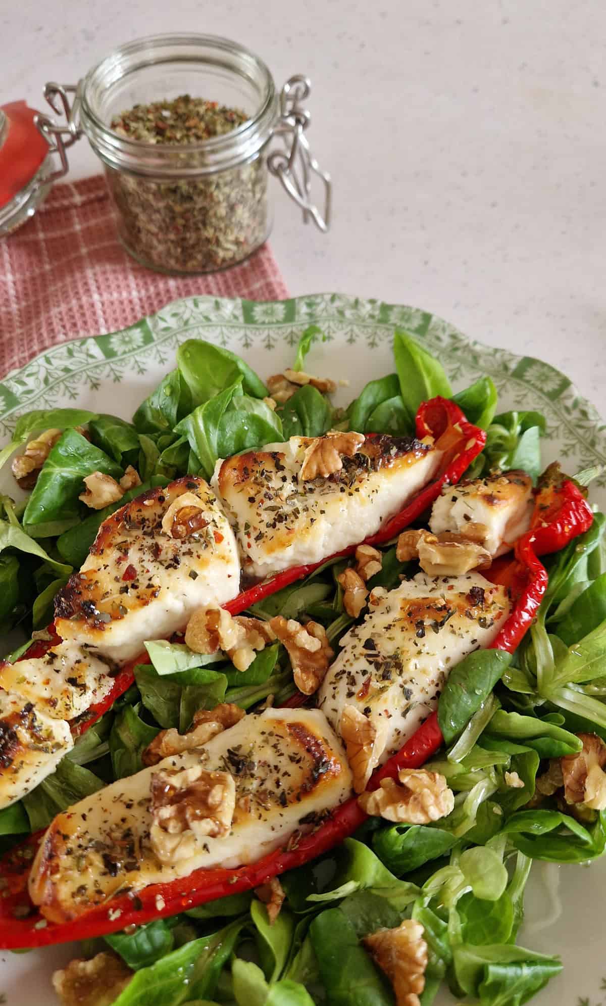 Een close-up van met geitenkaas gevulde paprika's. De groente ligt op een bedje van veldsla en is gegarneerd met walnoten.