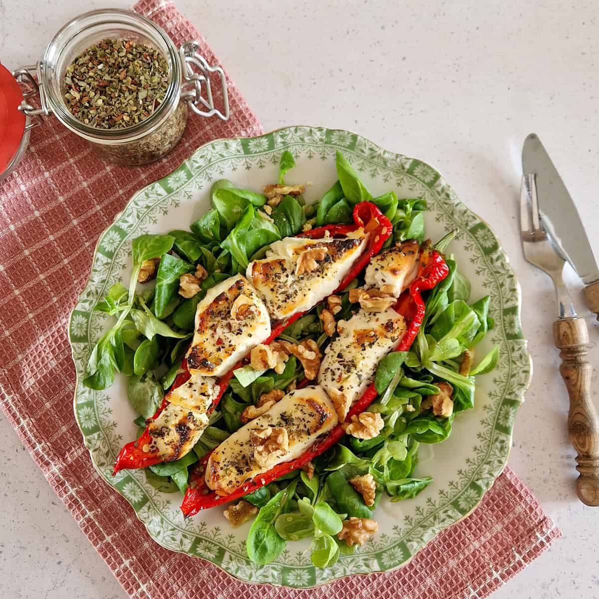 Gevulde puntpaprika's met geitenkaas en honing, op een bedje van veldsla. Het gerecht ligt op een ouderwets bordje met decoratieve groene rand.