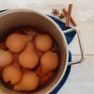 Chai stoofperen in een ruime pan. Naast de pan enkele smaakmakers van deze peertjes: steranijs en kaneel.