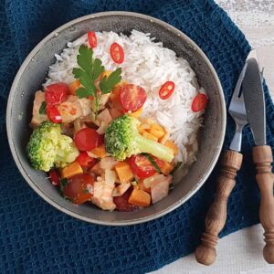 Curry met zalm en kokos, in de curry zit ook broccoli en wortel en het gerecht is gegarneerd met rode peper.