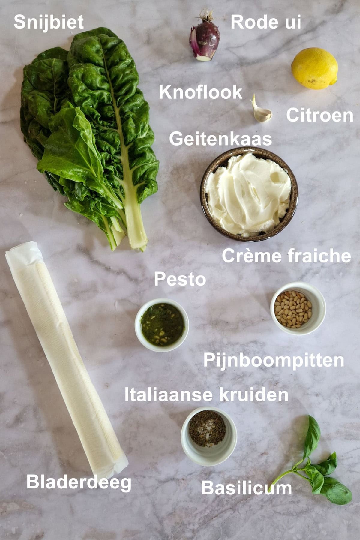 De ingrediënten voor snijbiet plaattaart, uitgestald op een marmeren ondergrond in een lichte tint.