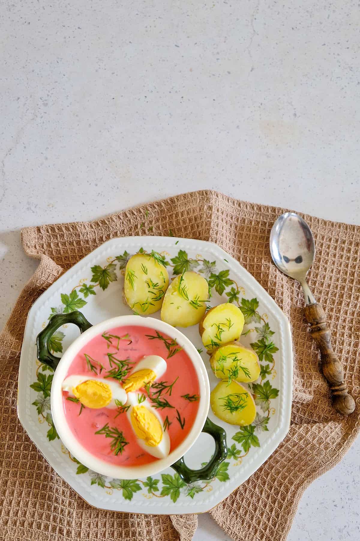 Šaltibarščiai - roze bietensoep uit Litouwen in een kom. De koude soep is gegarneerd met stukjes gekookt ei en verse dille en wordt geserveerd met gekookte aardappelen.