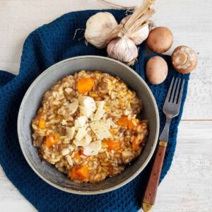 Risotto met pompoen in een grijze kom. Op de pompoenrisotto liggen flinters Parmezaanse kaas.