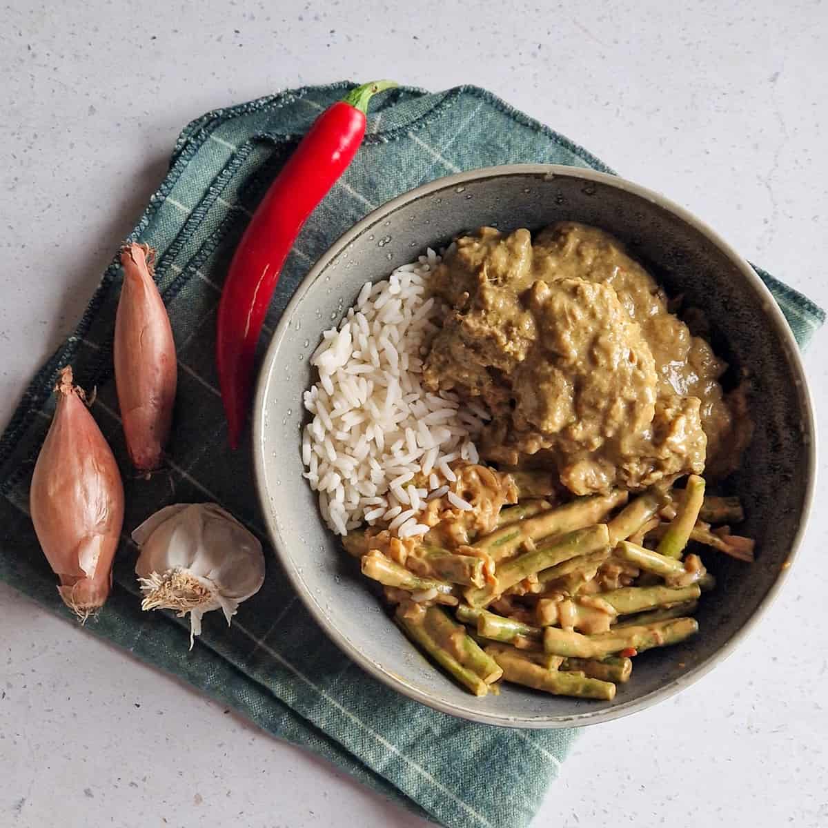 Een kommetje met rendang stoofvlees, rijst en boontjes.
