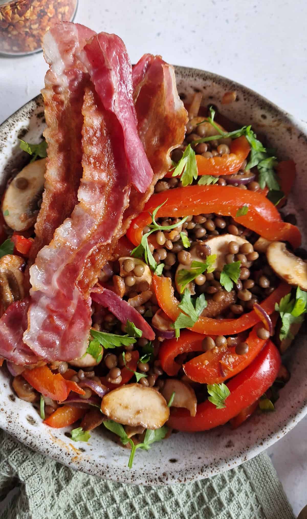 Een close-up van het gerecht zodat je de ingrediënten voor deze linzen met spek goed kunt zien: linzen, spek, paprika, champignons, rode ui en verse peterselie.