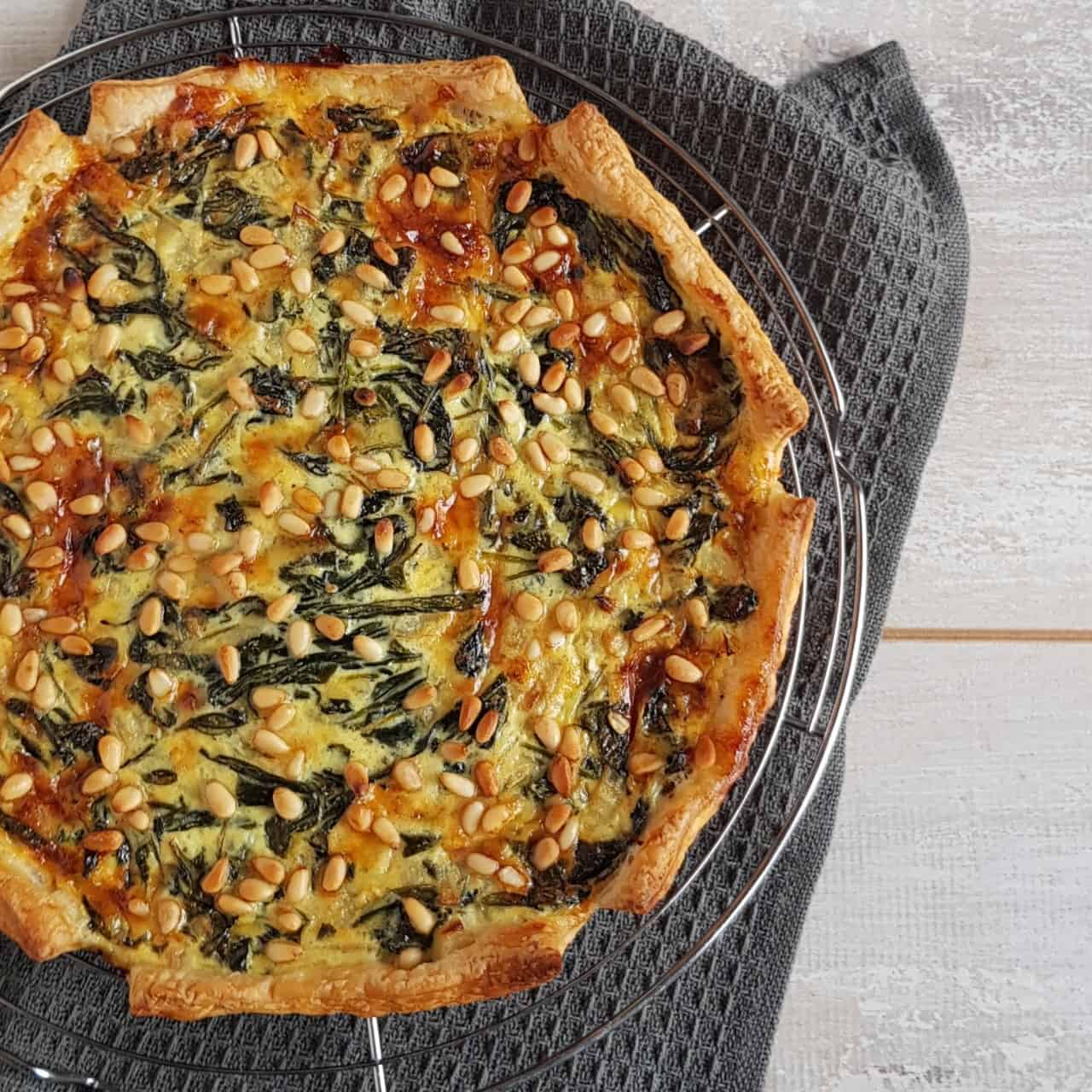 Quiche met spinazie en kaas, een bovenaanzicht van een rustieke quiche die ligt af te koelen op een ovenrek.