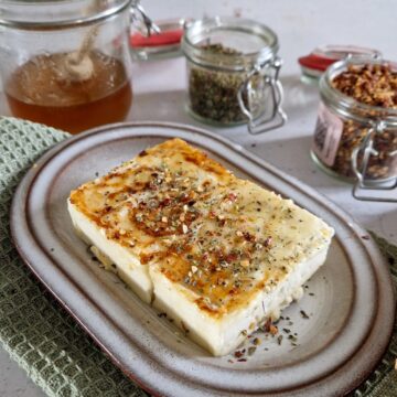 Saganaki - een stuk gebakken feta op een bordje. De feta is besprenkeld met honing, oregano en chilivlokken.