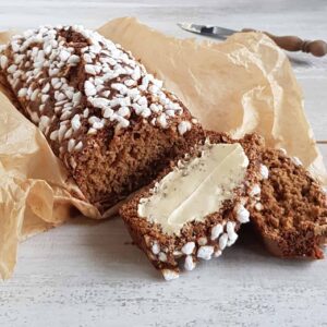 Ontbijtkoek: een zelfgebakken ontbijtkoek met parelsuiker in bakpapier gewikkeld. Er zijn twee plakken afgesneden, waarvan er één is besmeerd met boter.