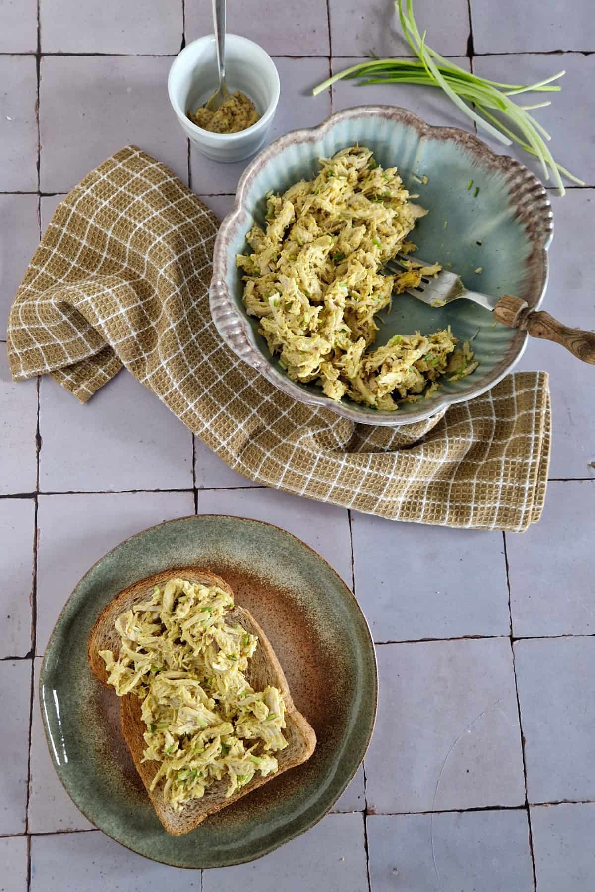 Een broodje met zelfgemaakte kip-kerrie salade. Op de achtergrond een kom met de rest van de salade.