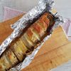 Stokbrood met mozzarella en geraspte kaas, uit de oven. Het stokbrood is verpakt in aluminiumfolie dat deels is opengevouwen.