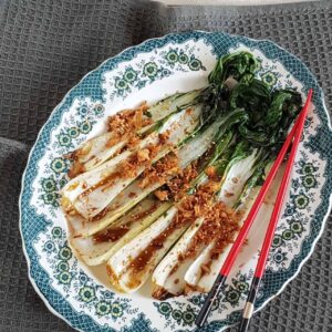 Paksoi roerbak met oestersaus op een decoratief blauw bord. De geroerbakte paksoi is bestrooid met gebakken uitjes en wit sesamzaad.