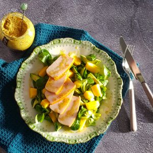 Salade met gerookte kip, mango en avocado op een groen bord. De zon geeft harde schaduwen op het gerecht, wat een speels effect geeft.
