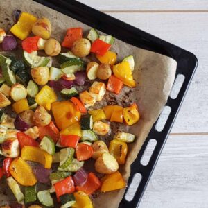Geroosterde groenten met halloumi en aardappels op een ovenplaat. De groenten zijn een mix van courgette, rode ui, gele paprika en rode paprika.