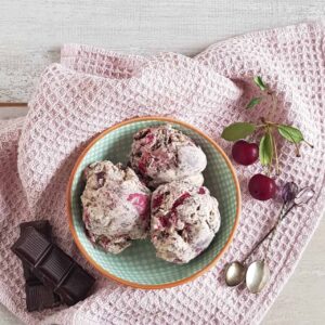 Drie bollen Cherry Garcia ijs in een serveerschaaltje. Naast het ijs liggen chocolade, kersen en lepeltjes.