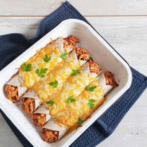 Pulled chicken wraps in een ovenschaal. De wraps zijn rijkelijk gevuld met pulled chicken en gegratineerd met een mengsel van cheddar en geraspte kaas.