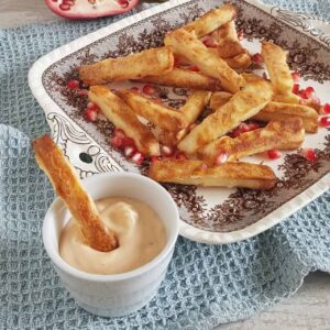 Halloumi frietjes op een bord met granaatappelpitjes. Eén van de frietjes staat in een bakje srirachamayonaise.