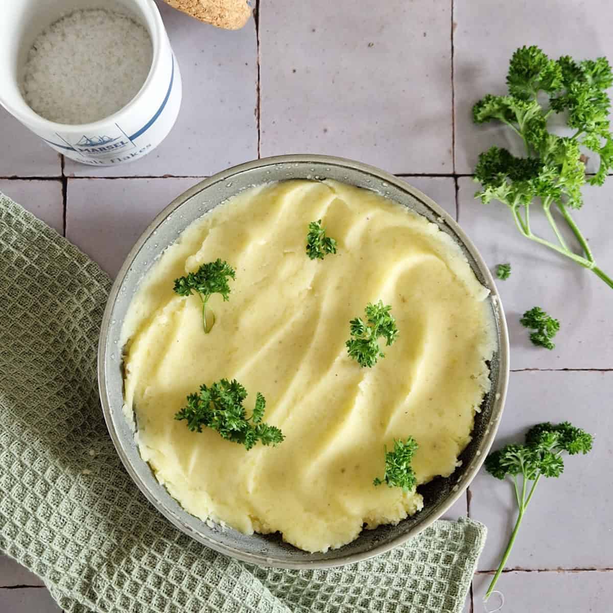 Aardappelpuree gegarneerd met verse peterselie. De puree zit in een kom die op een groene doek staat.