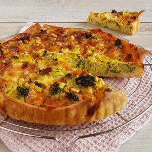 Quiche met broccoli en cheddar op een ovenrek. Er is een puntje uit de quiche gesneden zodat je de vulling goed kunt zien.