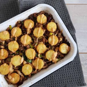 Shoarma ovenschotel - een bovenaanzicht. De shoarmaschotel is belegd met kleine rostirondjes en besprenkeld met een pittige saus.