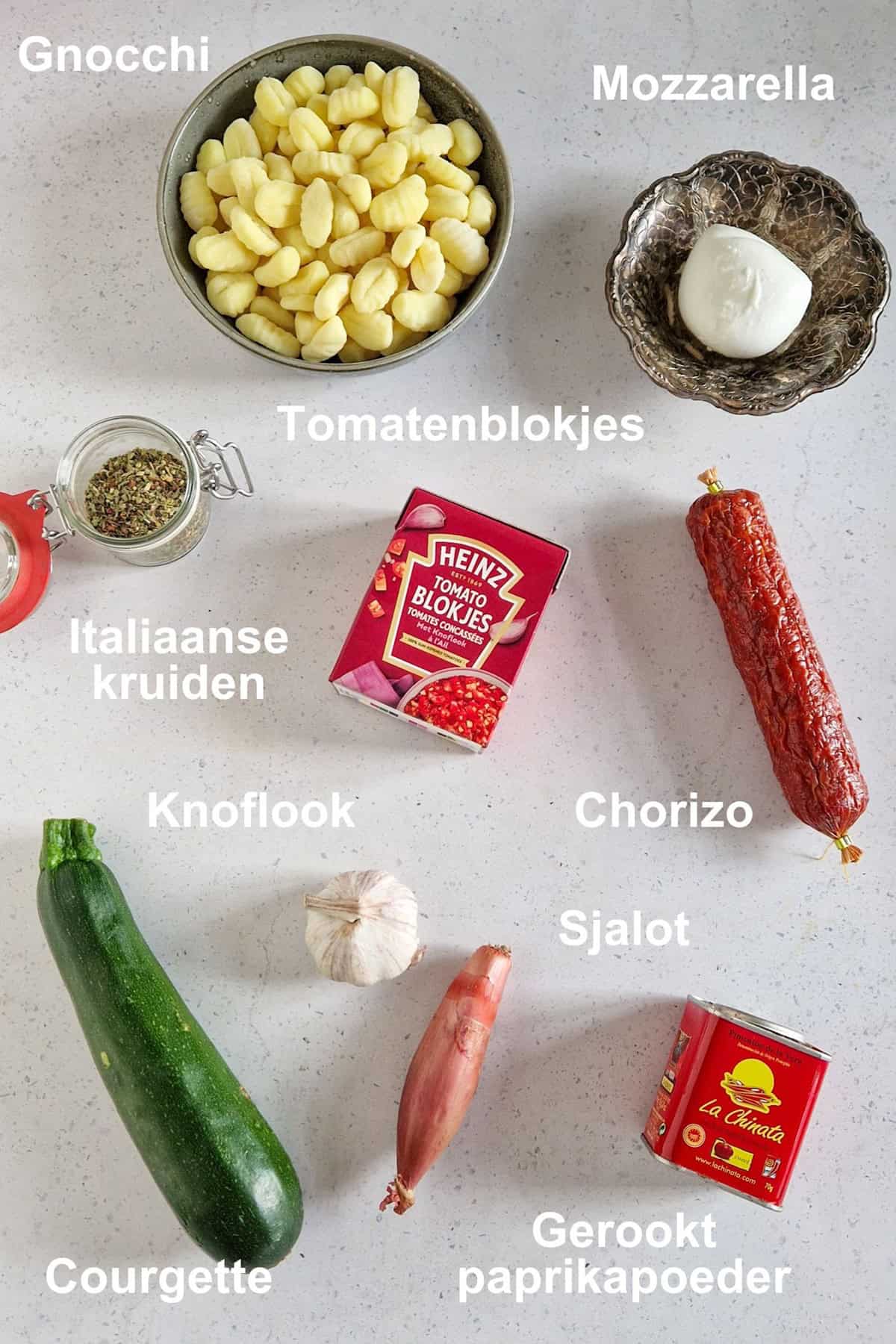 De ingrediënten om een gnocchi ovenschotel met chorizo te maken, uitgestald op een wit-marmeren ondergrond.