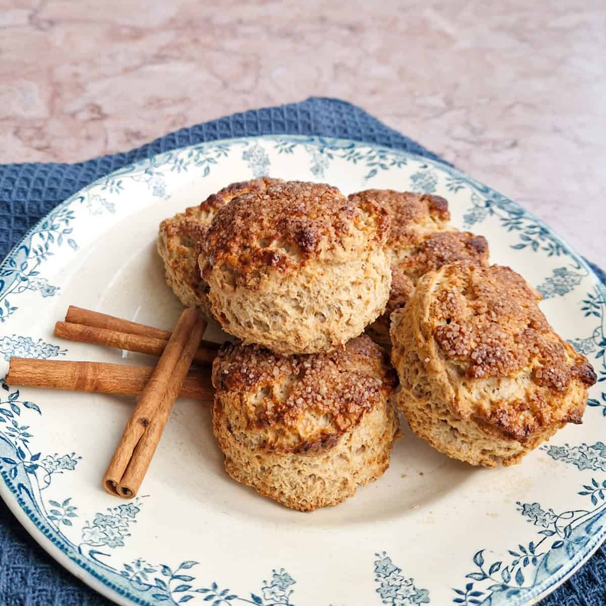 Een stapeltje kaneelscones op een bordje met een ouderwetse blauwe rand. Er liggen kaneelstokjes bij.