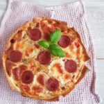 Pizza quiche: bovenaanzicht van een quiche met plakjes salami en pizzakruiden. De quiche is gegarneerd met verse basilicum.