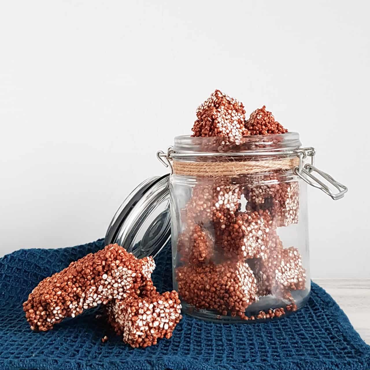 Quinoarepen van gepofte quinoa met chocolade. De repen zitten in een grote glazen pot met een openstaand deksel.