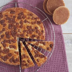 Stroopwafel boterkoek op een ovenrek. Er zijn drie puntjes uit de boterkoek gesneden. De foto is een bovenaanzicht waardoor je de stukjes stroopwafel op de boterkoek goed kunt zien.