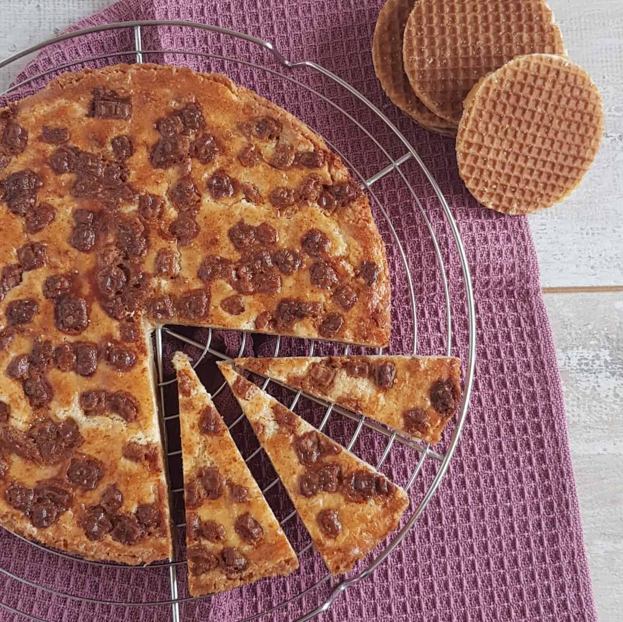 Stroopwafel boterkoek op een ovenrek. Er zijn drie puntjes uit de boterkoek gesneden. De foto is een bovenaanzicht waardoor je de stukjes stroopwafel op de boterkoek goed kunt zien.