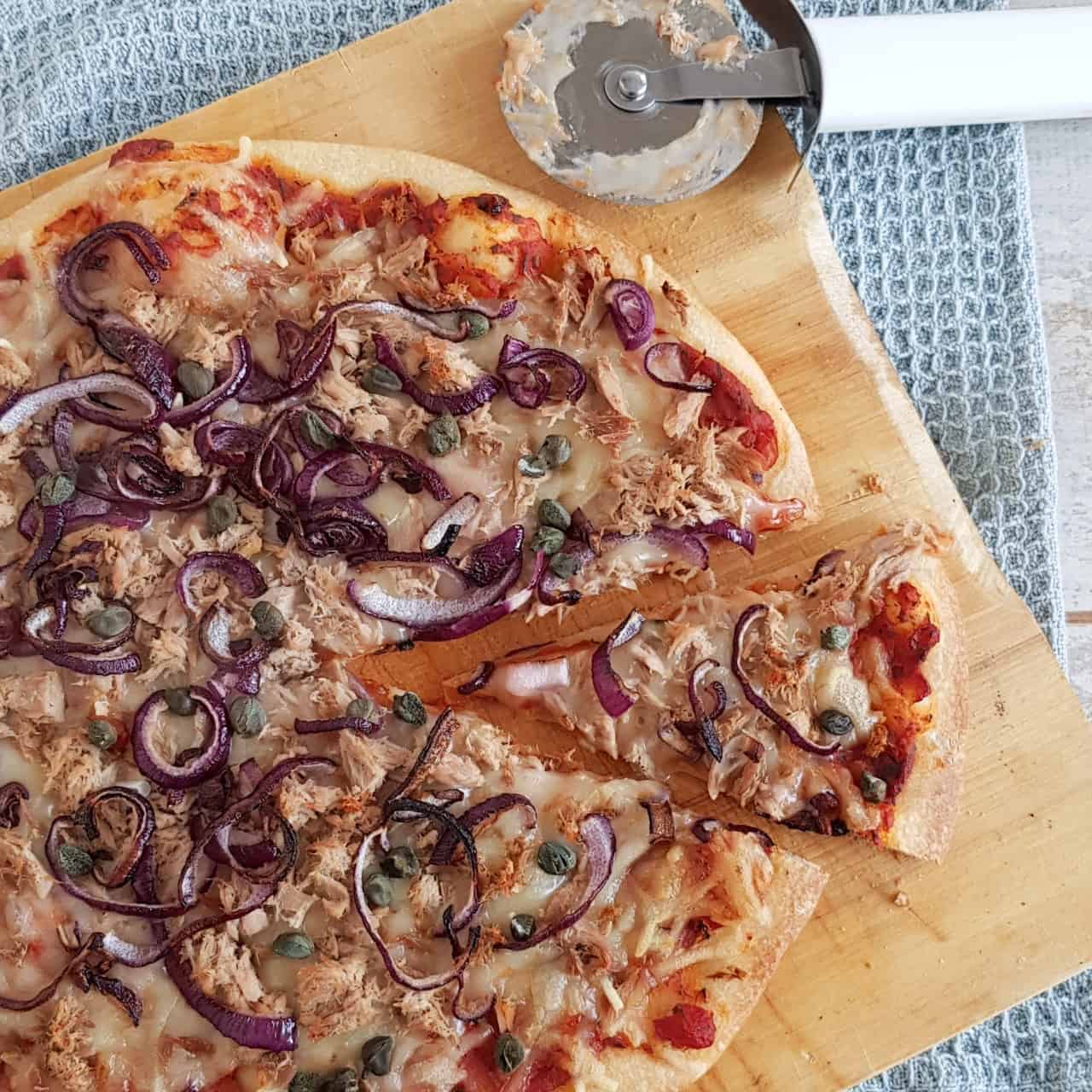 Pizza tonijn - pizza tonno met een puntje eruit gesneden. De tonijnpizza is rijkelijk belegd met tonijn, rode uit en kappertjes.
