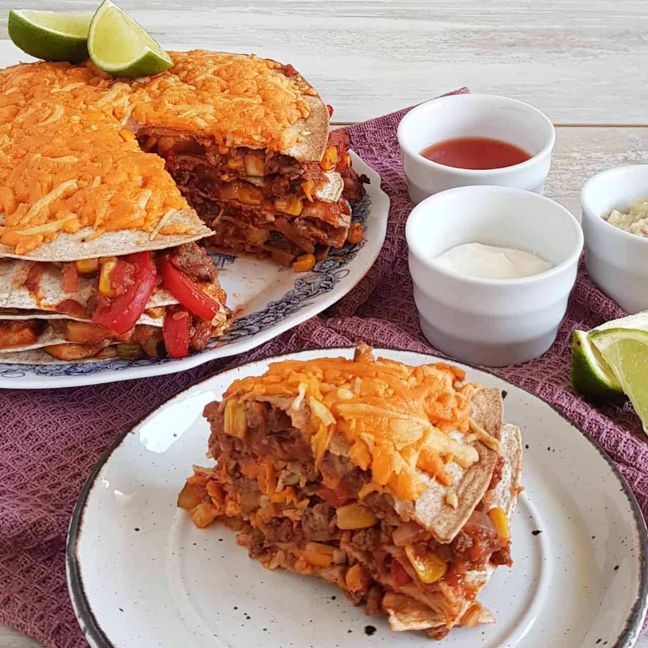 Tortillataart - Mexicaanse wraptaart. Uit de taart is een punt gesneden die op een bordje ligt, waardoor je de rijke vulling van gehakt, paprika, mais en geraspte kaas goed kunt zien.