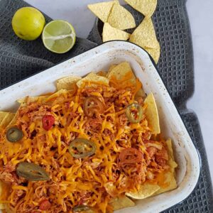 Pulled chicken nachos met geraspte cheddar en jalapenos, in een ovenschaal.