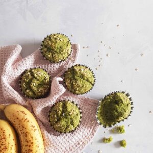 Spinaziemuffins met banaan op een lichtroze doek. Eén van de muffins is verkruimeld voor een speels effect.