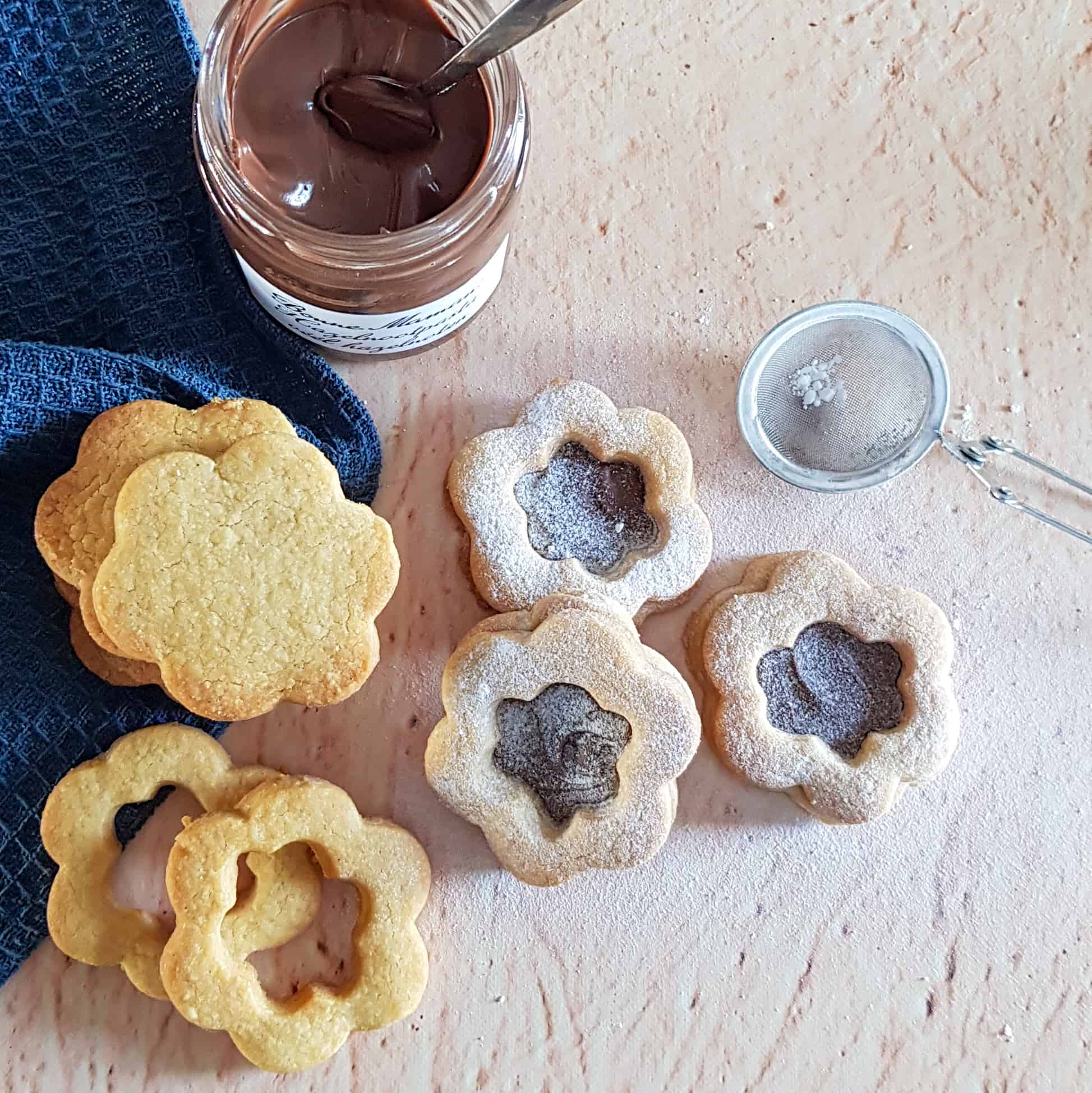 Zandkoekjes met hazelnootpasta: de koekjes bestaan uit een bloemvormig deeg met daarop een laagje hazelnootpasta. De koekjes zijn afgedekt met een koekje met een gat in de vorm van een bloem, zodat de vulling goed zichtbaar is.