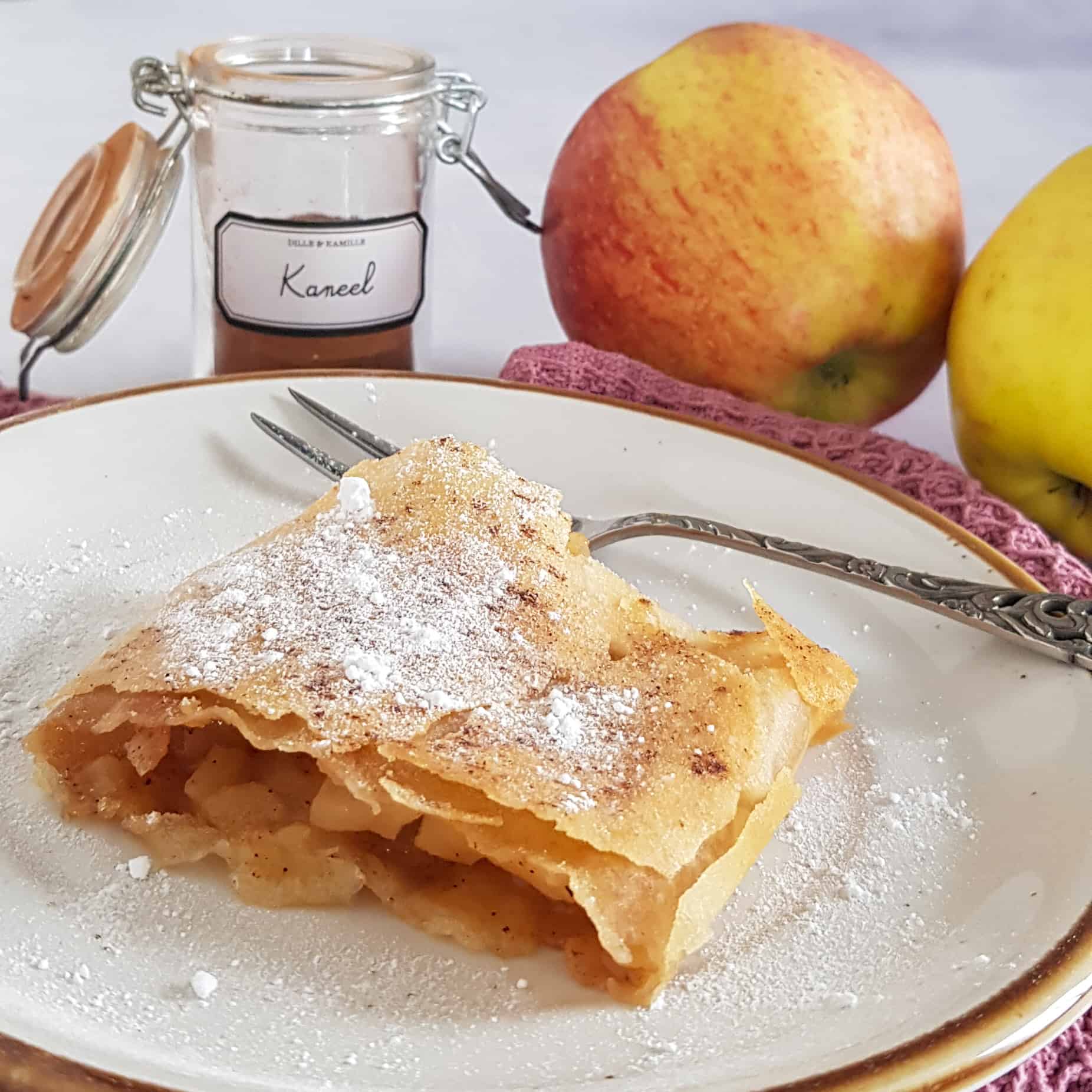 Apfelstrudel op een gebaksbordje. De apfelstrudel is bestrooid met poedersuiker en kaneel.